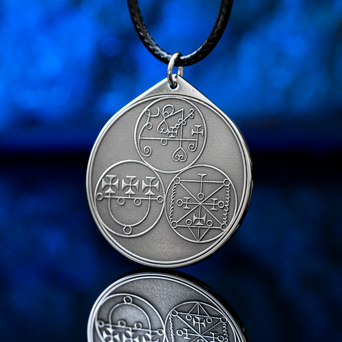 Reverse side of the Feline Goetic Trinity pendant with three engraved demon sigils of Sitri, Ose and Beleth from the Ars Goetia. Silver-tone Goetic talisman necklace on a black cord against a blue background.