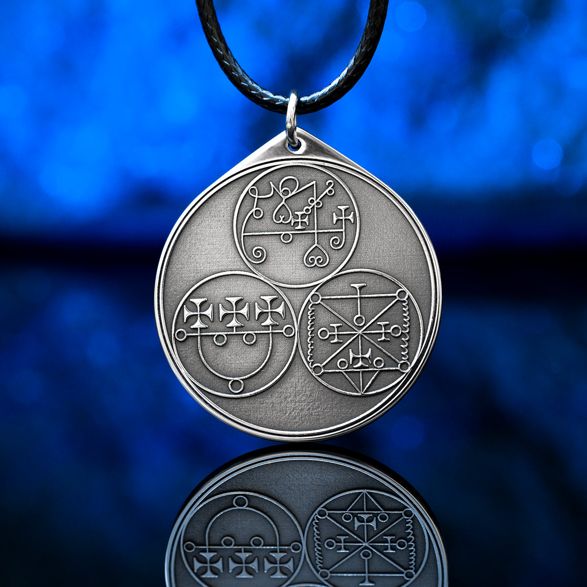 Reverse side of the Feline Goetic Trinity pendant with three engraved demon sigils of Sitri, Ose and Beleth from the Ars Goetia. Silver-tone Goetic talisman necklace on a black cord against a blue background.