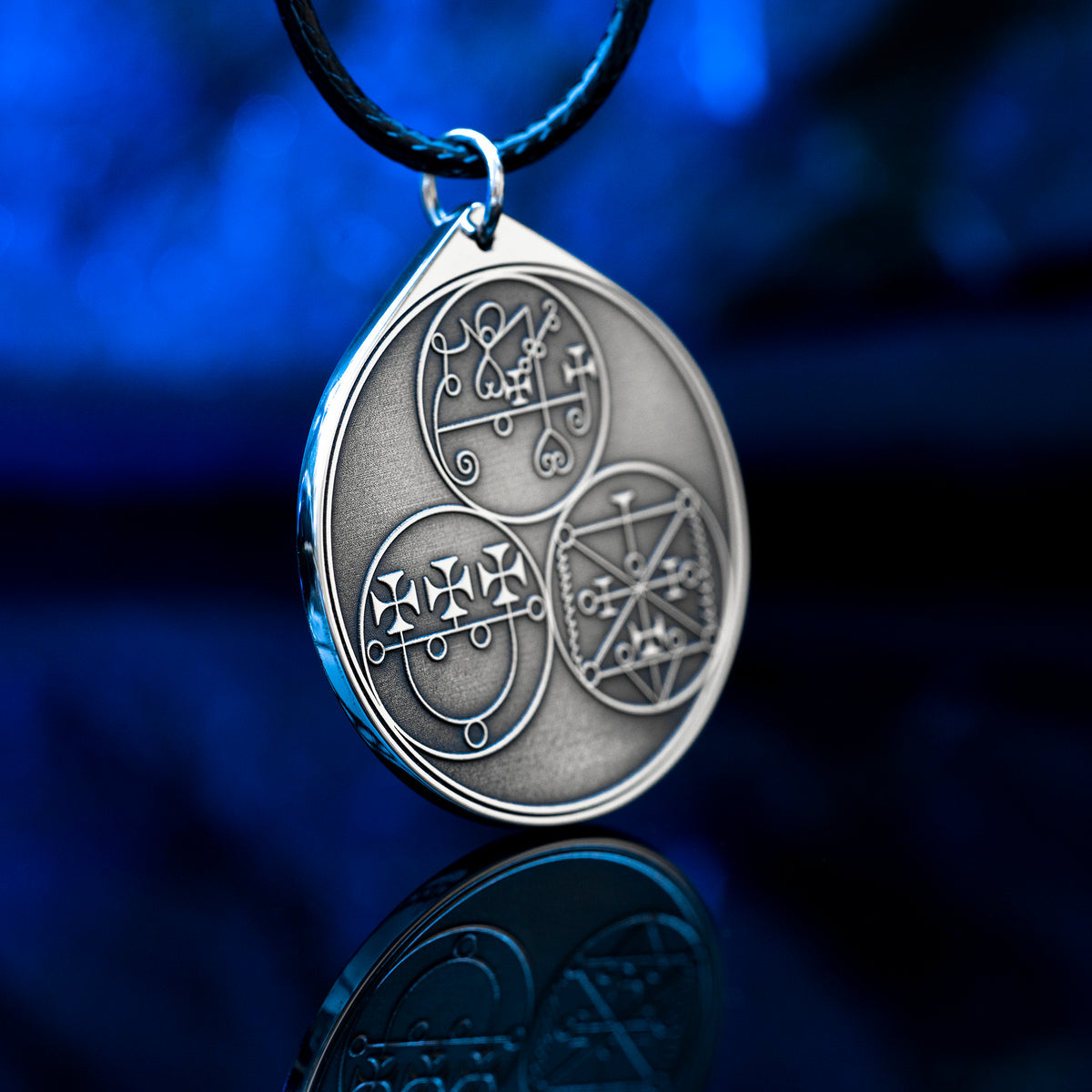 Reverse side of the Feline Goetic Trinity pendant with three engraved demon sigils of Sitri, Ose and Beleth from the Ars Goetia. Silver-tone Goetic talisman necklace on a black cord against a blue background.