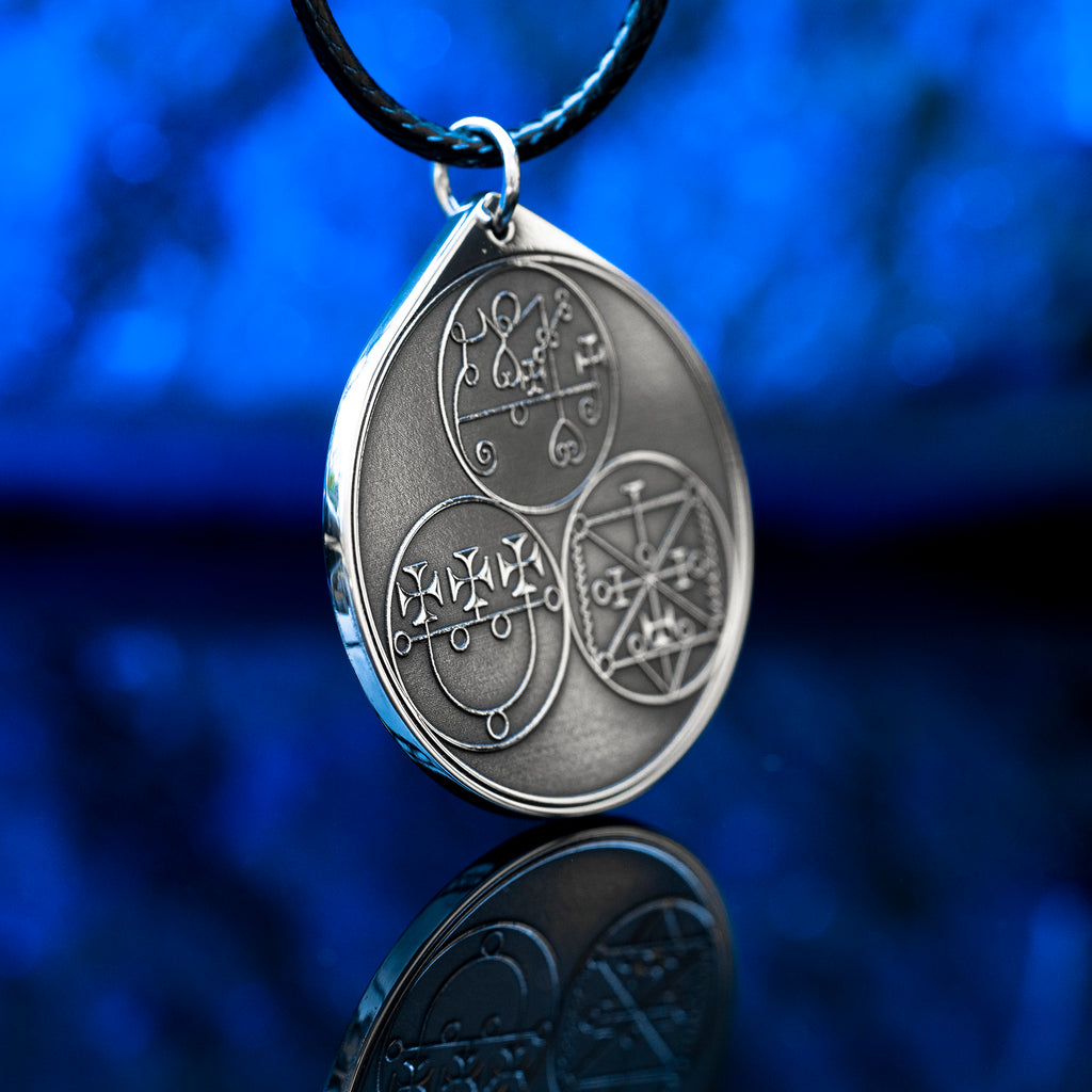 Reverse side of the Feline Goetic Trinity pendant with three engraved demon sigils of Sitri, Ose and Beleth from the Ars Goetia. Silver-tone Goetic talisman necklace on a black cord against a blue background.