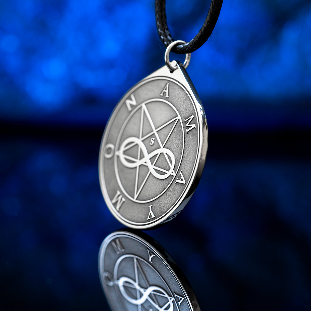 Amaymon Seal Pendant featuring an engraved inverted pentagram, intertwined infinity symbol and Amaymon lettering. Round silver tone occult medallion on a black braided cord, photographed against a deep blue background with a reflection