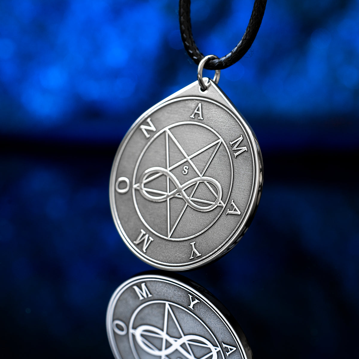 Amaymon Seal Pendant featuring an engraved inverted pentagram, intertwined infinity symbol and Amaymon lettering. Round silver tone occult medallion on a black braided cord, photographed against a deep blue background with a reflection
