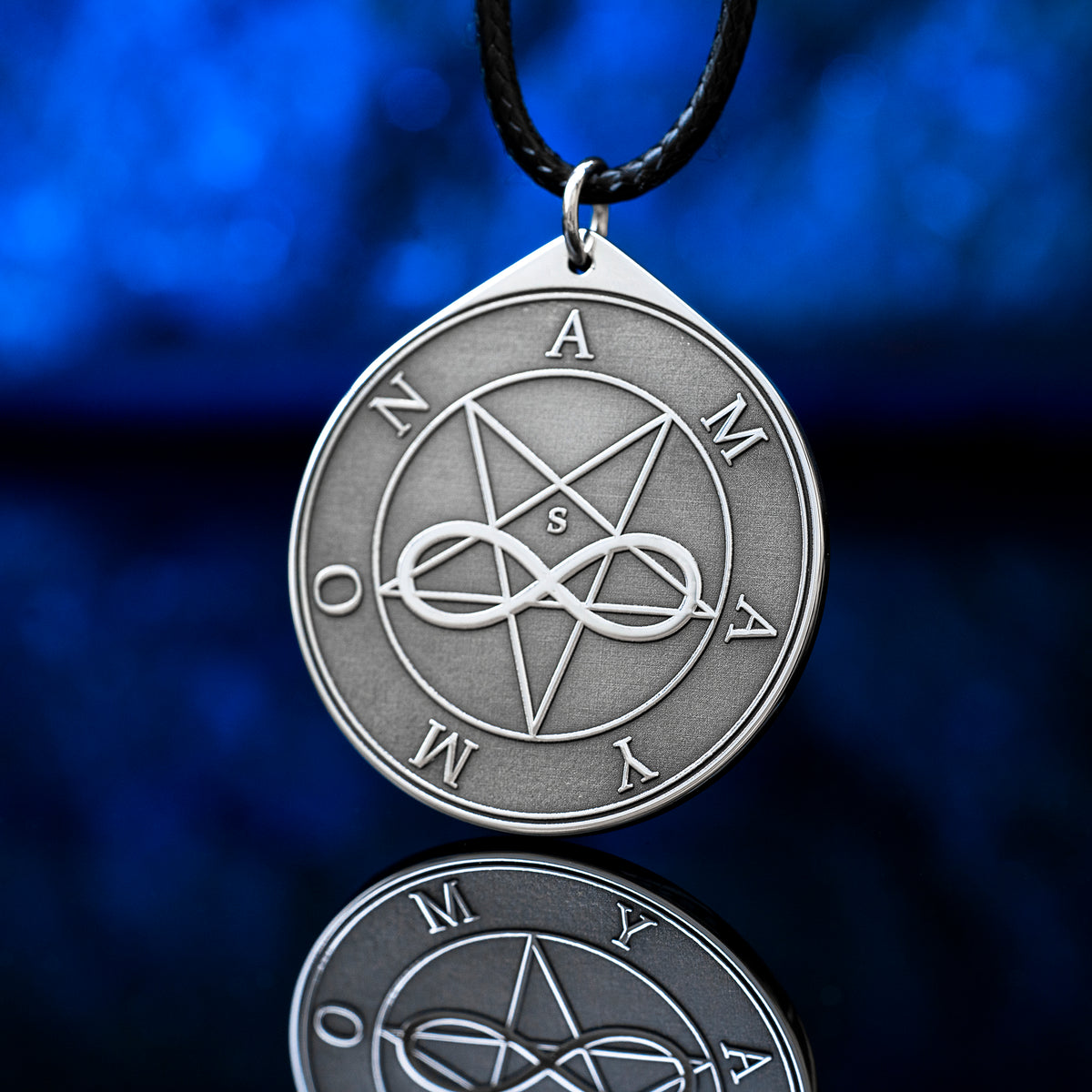 Amaymon Seal Pendant featuring an engraved inverted pentagram, intertwined infinity symbol and Amaymon lettering. Round silver tone occult medallion on a black braided cord, photographed against a deep blue background with a reflection