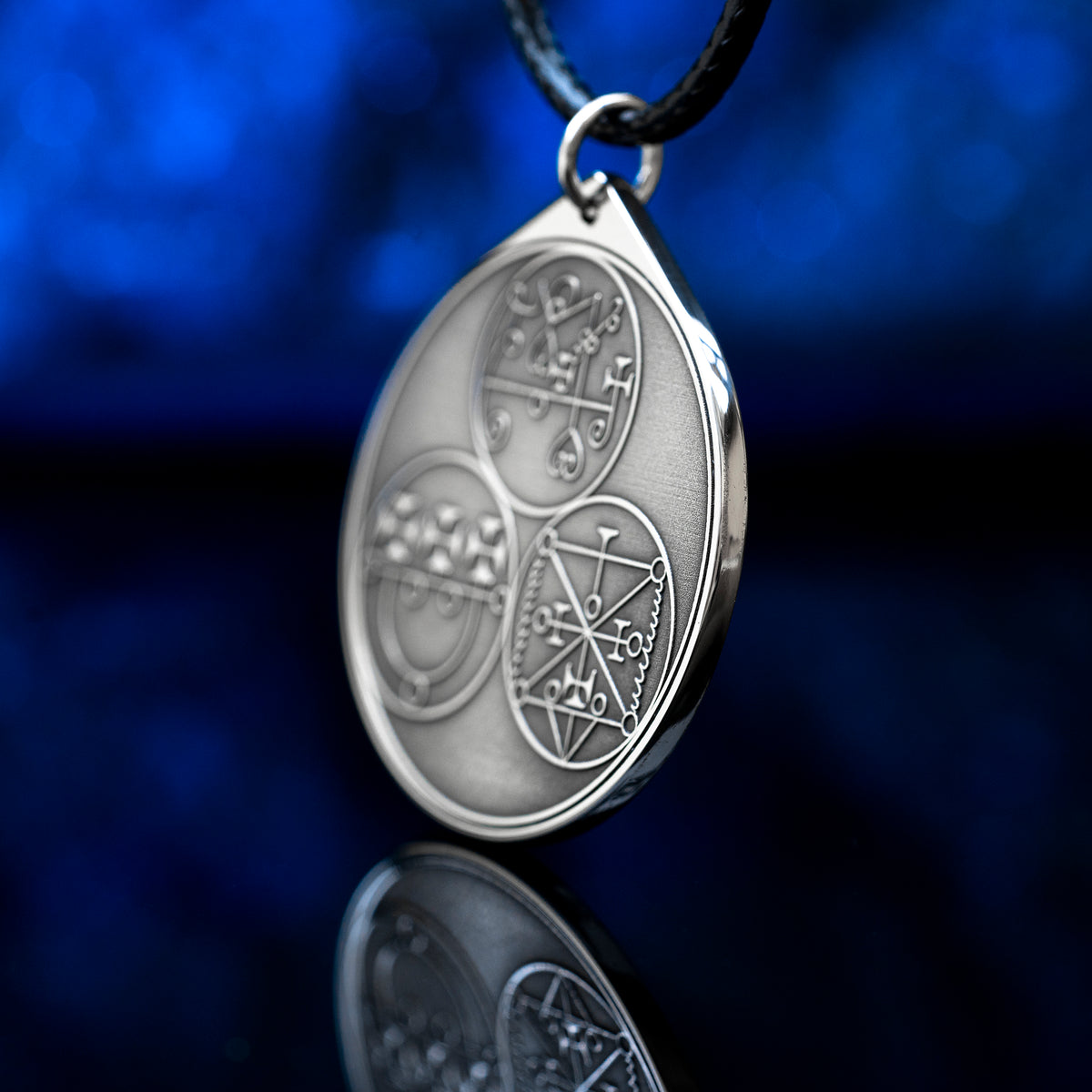 Reverse side of the Feline Goetic Trinity pendant with three engraved demon sigils of Sitri, Ose and Beleth from the Ars Goetia. Silver-tone Goetic talisman necklace on a black cord against a blue background.