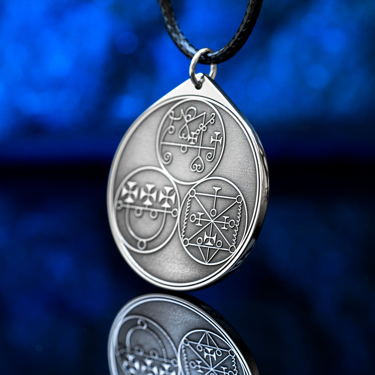 Reverse side of the Feline Goetic Trinity pendant with three engraved demon sigils of Sitri, Ose and Beleth from the Ars Goetia. Silver-tone Goetic talisman necklace on a black cord against a blue background.